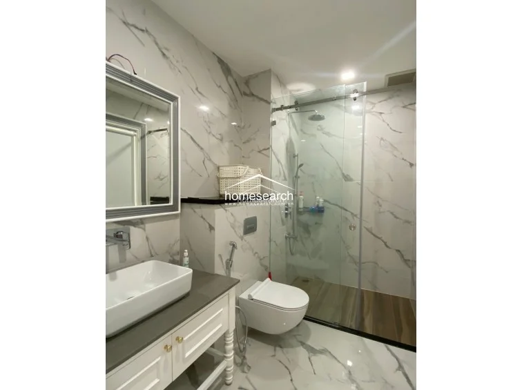 This modern bathroom is elegantly appointed with white marble-vein wall tiles and a sleek, wall-mounted vanity with a vessel sink. It includes a glass-enclosed walk-in shower and a wall-hung toilet, reflecting a high standard of maintenance and contemporary design.