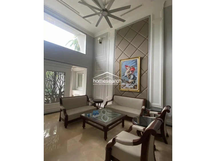 This expansive living room highlights the architectural drama of the double-height ceiling and large upper windows that flood the space with natural light. The room is decorated with a sophisticated mix of neutral tones, ornate wall molding, and a decorative screen, creating a refined and airy atmosphere.