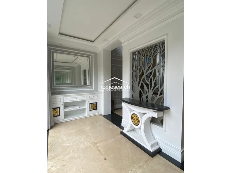 This transition space showcases sophisticated architectural details, including a decorative tree-motif room divider and a built-in console with a black marble top. The area is brightened by a large mirror and recessed ceiling lighting, maintaining a cohesive, upscale aesthetic with polished tile floors.