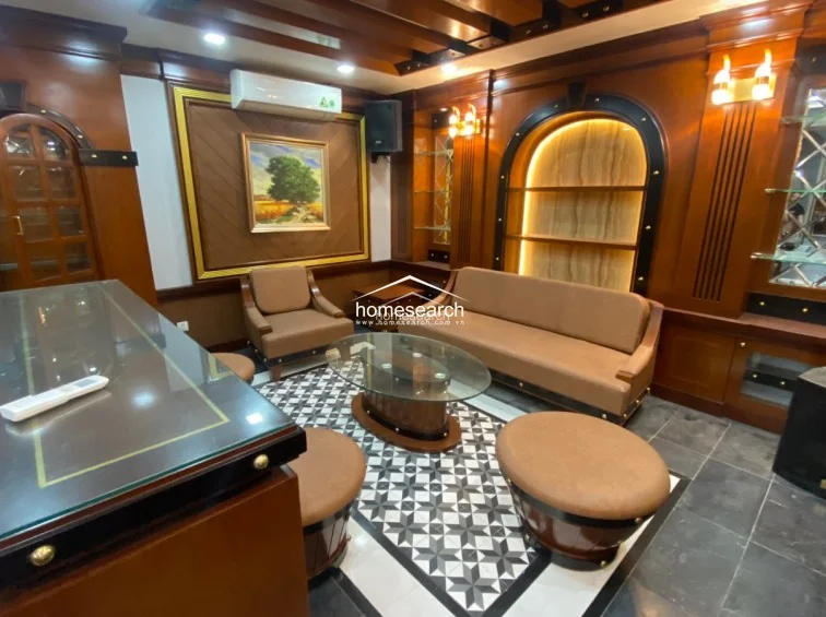 This lounge area is an extension of the formal space, featuring a comfortable sofa and armchairs arranged around a glass-topped coffee table. The room is heavily accented with rich wood paneling, arched display niches with warm backlighting, and a wall-mounted AC unit for climate control.