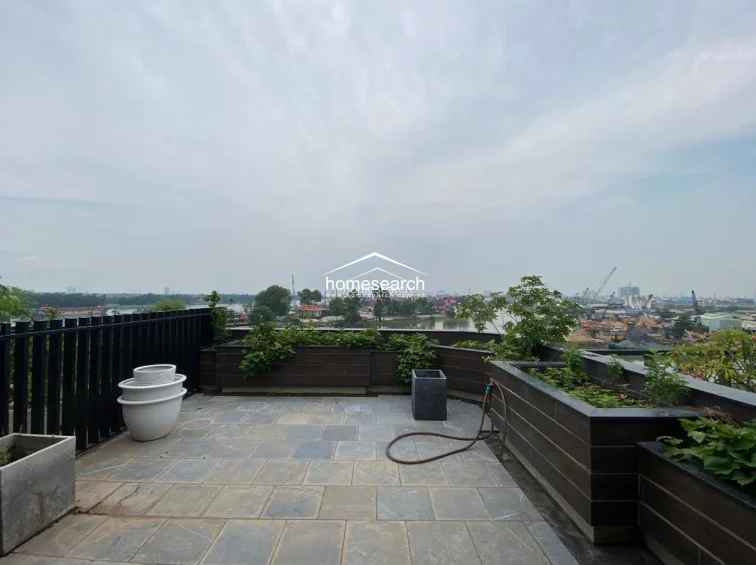 This terrace space is designed for low-maintenance outdoor living, featuring grey stone-look floor tiles and built-in planters that define the perimeter. A black metal railing provides safety while maintaining the open feel, and the area is equipped with a garden hose for easy upkeep.