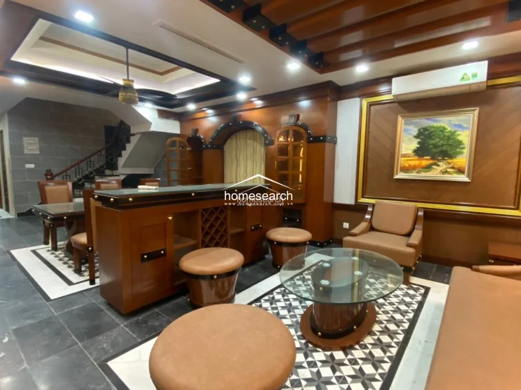 This view highlights the transition between the dining and lounge zones, showcasing the cohesive use of dark wood paneling and decorative ceiling beams throughout the interior. The space is highly organized with built-in wine racks, display cabinets, and a consistent, elegant design aesthetic that appears to be in excellent condition.