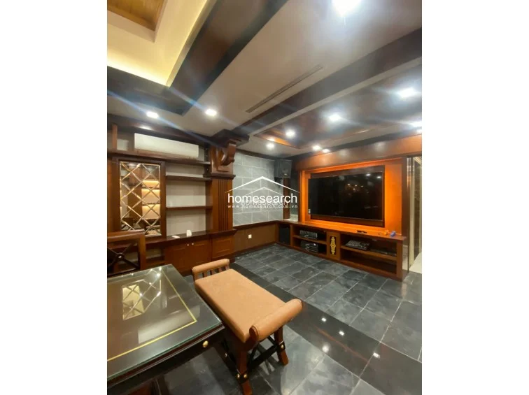 This room serves as a formal media or entertainment lounge, characterized by extensive dark wood paneling, built-in shelving, and a large wall-mounted television. The space features dark stone floor tiles, recessed ceiling lighting, and a wall-mounted air conditioning unit, creating a sophisticated and enclosed atmosphere.