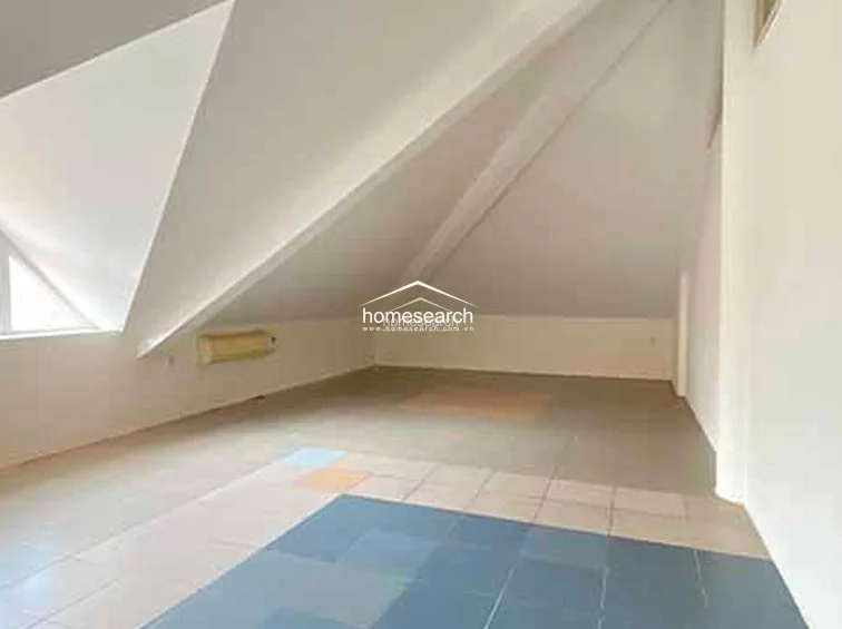 This attic-style room features a dramatic sloped ceiling and a clean, minimalist aesthetic with white walls. The space is finished with large, multi-toned square floor tiles and includes a wall-mounted AC unit for climate control.