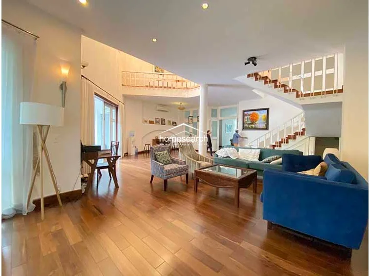 This wide-angle view highlights the impressive double-height ceiling and the sophisticated, open-concept layout of the main living space. The area is well-furnished with a mix of contemporary seating, including a bold blue sofa, and is illuminated by a combination of natural light from large windows and stylish wall sconces.