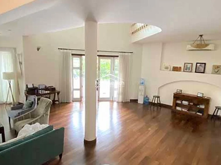 This expansive living area features rich wood flooring and a prominent central column, creating an open-concept flow that connects to the dining and entry spaces. The room is highlighted by high ceilings, a decorative arched wall niche for display, and large glass doors that invite abundant natural light.
