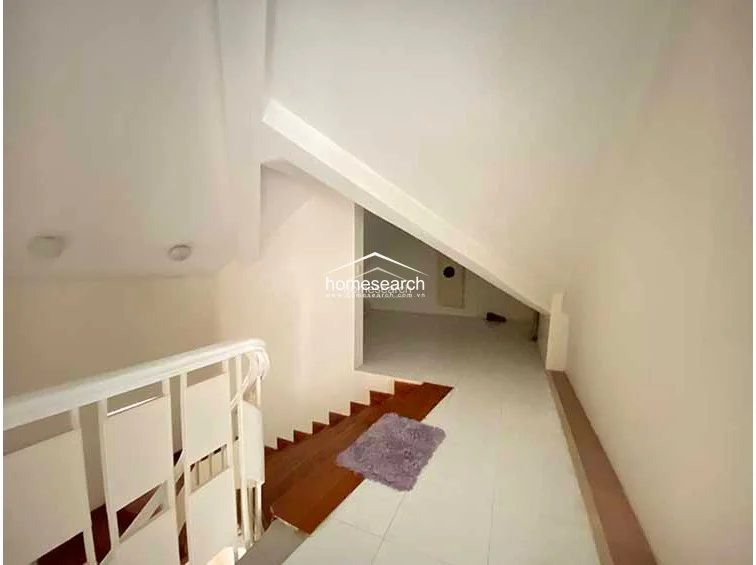 This landing area connects to the upper level via a white-railed staircase, transitioning from hardwood steps to tiled flooring. The space is characterized by a dramatic sloped ceiling and a clean, white color scheme, providing a bright and airy transition between floors.