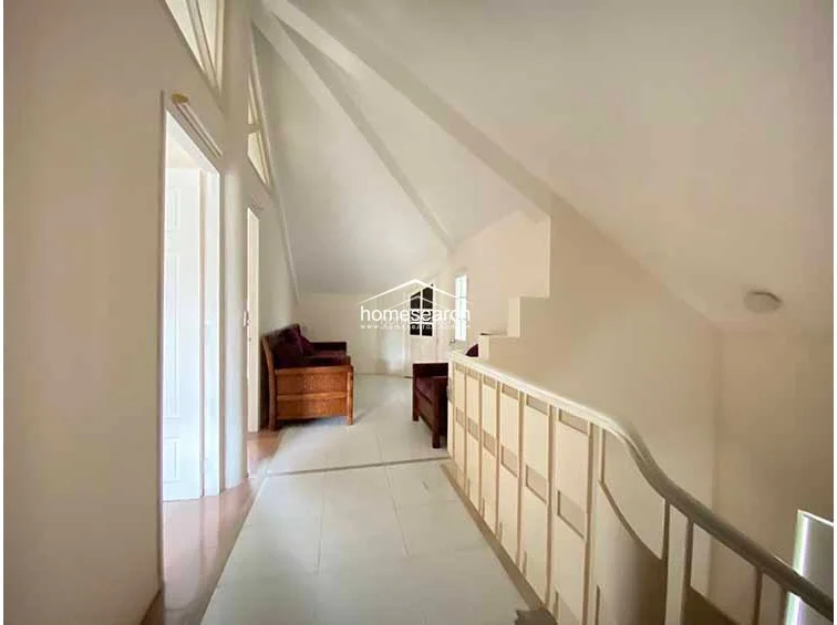 This image shows an attic-style hallway with a vaulted ceiling and white walls, creating a bright and airy atmosphere. The space features a simple staircase with a white railing and connects to multiple rooms, with light-colored tile flooring throughout.