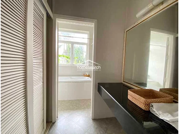 This bathroom vanity area is finished with a sleek black countertop and a large, gold-framed mirror that enhances the sense of space. It includes a convenient storage closet with louvered doors and offers a clear view into the adjacent room, which houses a large soaking tub.