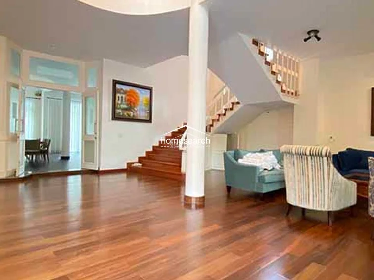 The living room layout is defined by a large structural column, with a comfortable seating arrangement positioned to enjoy natural light from the expansive floor-to-ceiling windows. The room maintains a sophisticated, well-maintained aesthetic, complemented by recessed lighting and a wall-mounted air conditioning unit.