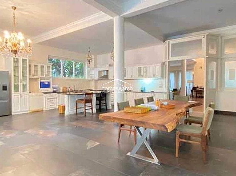 The kitchen area is bright and functional, featuring extensive white cabinetry, a built-in oven, and a clean, minimalist design that flows directly into the dining area. The space is well-lit by both natural light and elegant hanging chandeliers, maintaining a high standard of maintenance and a cohesive, bright color scheme.