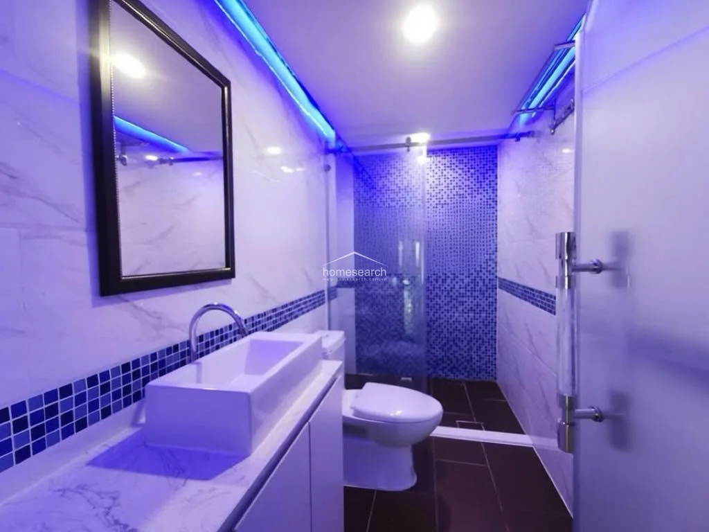 This modern bathroom is finished with marble-style wall tiles and a vibrant blue mosaic accent wall in the walk-in shower area. It is equipped with a contemporary vessel sink, a glass shower enclosure, and dramatic blue LED strip lighting that creates a high-end, spa-like atmosphere.
