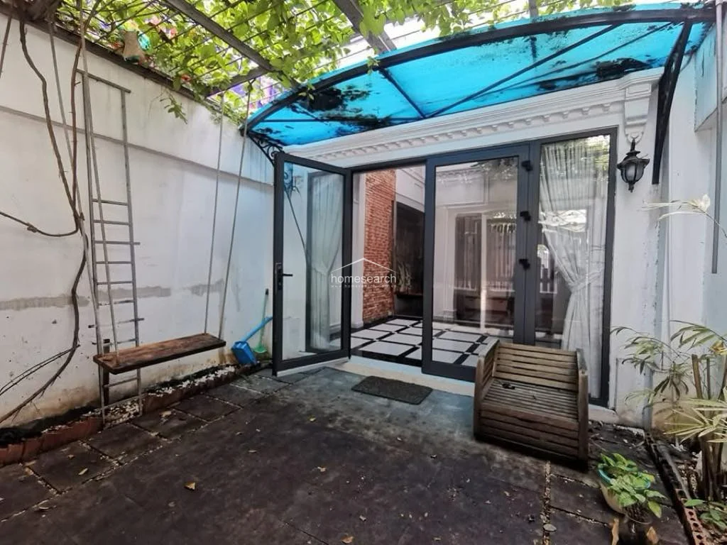 This outdoor terrace serves as a private retreat, featuring a rustic wooden swing and a cozy seating area beneath a lush, vine-covered pergola. It connects to the interior living space through large, modern glass-paned doors, which allow for seamless indoor-outdoor flow and natural light.