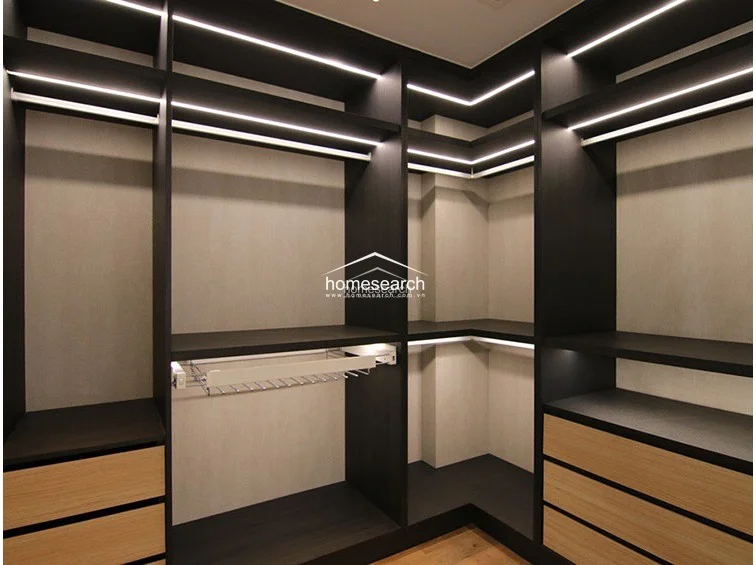This custom walk-in closet is expertly organized with dark wood shelving and integrated LED strip lighting for a sophisticated, high-end feel. It features a mix of hanging rods, open shelving, and light wood-finished drawers, providing ample storage space in a compact, functional layout.