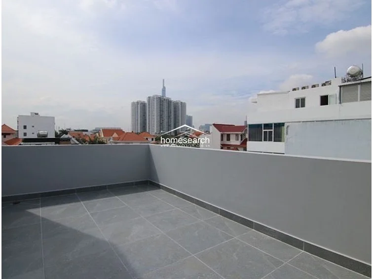 This open-air terrace offers a panoramic urban view, including a prominent skyscraper, and is finished with durable grey floor tiles and matching perimeter walls. The space is well-maintained and provides a clean, private outdoor area suitable for relaxation or entertaining.