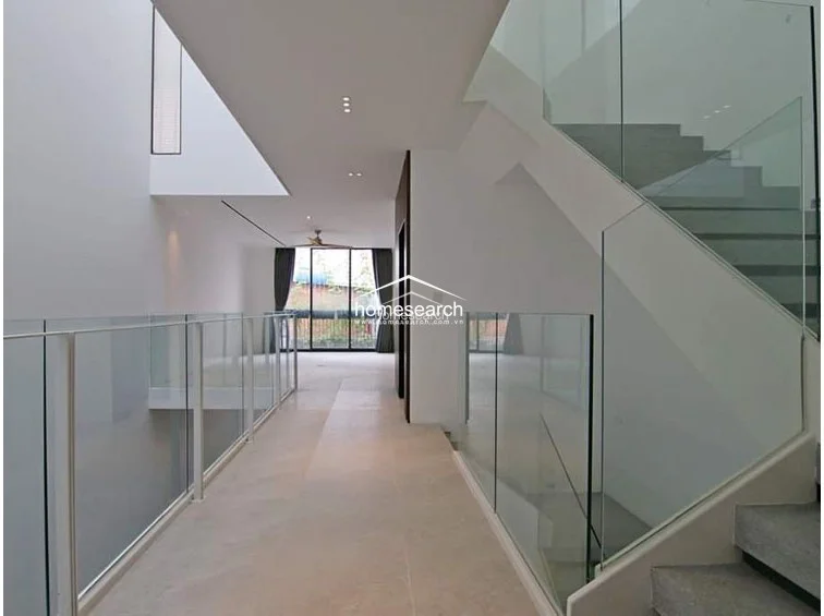 This perspective showcases the architectural drama of the home, featuring a long, light-filled hallway that overlooks the lower levels through glass partitions. The design emphasizes verticality and openness, with a staircase that serves as a sculptural element against the neutral, minimalist backdrop. The property appears to be in pristine condition, reflecting a high-end, modern architectural style with an emphasis on light and spatial connectivity.