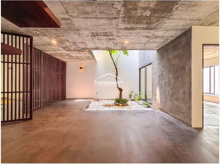 This perspective highlights the open-plan ground floor, showing the flow from the front entrance through to the central courtyard and rear living zones. The use of floor-to-ceiling wooden slats and raw concrete textures creates a cohesive, high-end industrial atmosphere that is well-maintained and architecturally distinct.