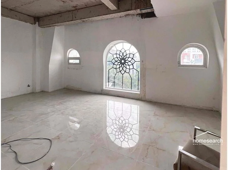 This unfinished attic-style room features striking architectural details, including arched windows with decorative black metal grilles and high, sloped ceilings. The space is finished with large, polished light-colored floor tiles, offering a blank canvas with significant potential for a unique living area or studio.