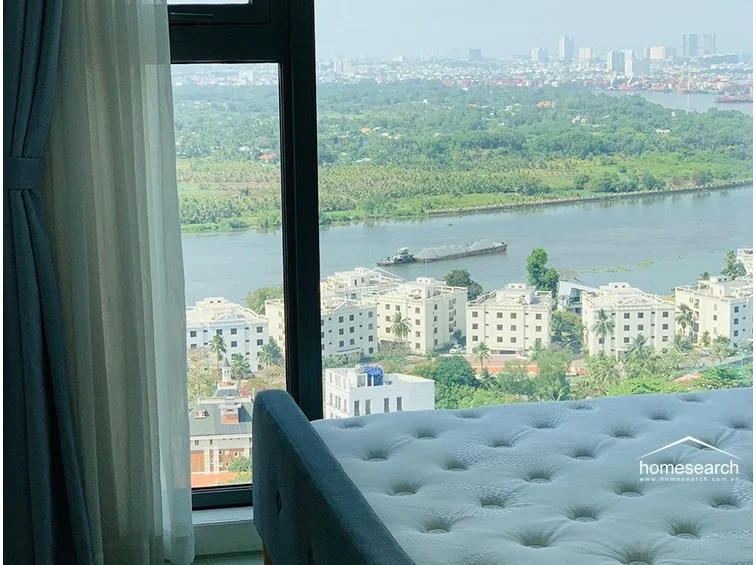 This bedroom features a floor-to-ceiling window that offers a panoramic river view and abundant natural light. The room is finished with light wood-style flooring and neutral wall tones, creating a clean and modern aesthetic.