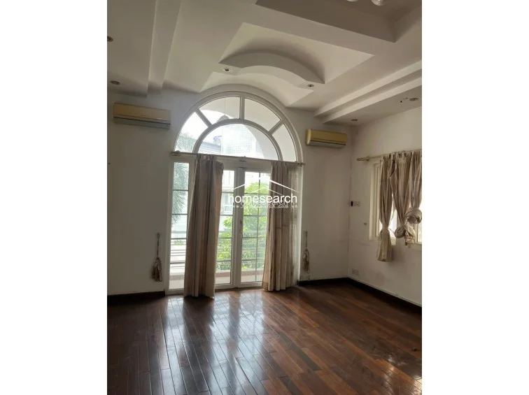This bright living space is defined by an elegant arched window and door combination that provides ample natural light and outdoor access. The room showcases a sophisticated tray ceiling design and dark hardwood floors, creating a spacious and well-ventilated atmosphere.