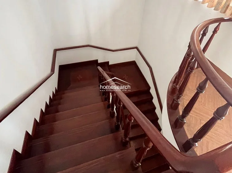 This close-up captures the elegant craftsmanship of the dark wood staircase, which features a curved handrail and classic balusters. The landing is finished with high-quality hardwood flooring, showcasing a refined, traditional design aesthetic.