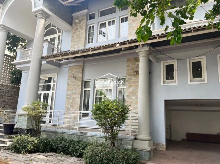 The side profile of the residence highlights a spacious covered carport area and large window placements that allow for natural light. The structure maintains a consistent aesthetic with its blue facade and stone detailing, though the building exterior shows signs of weathering that will need attention.