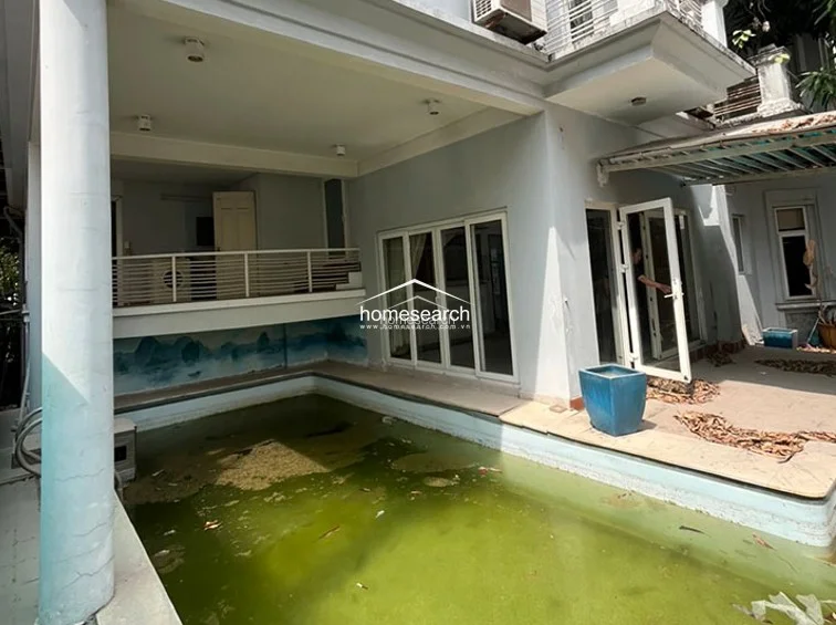 The rear terrace provides a direct view of the swimming pool, which is currently filled with stagnant water and debris. The space is finished with tile flooring and features a mural on the lower wall, but the entire outdoor area is in need of deep cleaning and maintenance to restore its functionality.