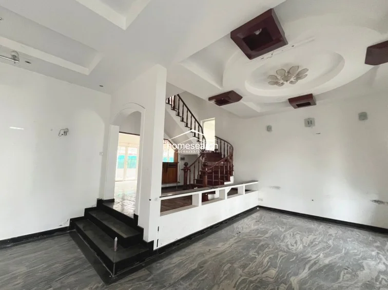 This spacious area serves as a central hub, showcasing a dramatic spiral wooden staircase and a low-profile partition wall that defines the transition between levels. The floor is finished in a striking grey-toned marble, while the ceiling features intricate circular molding and recessed lighting, creating a sophisticated architectural focal point.