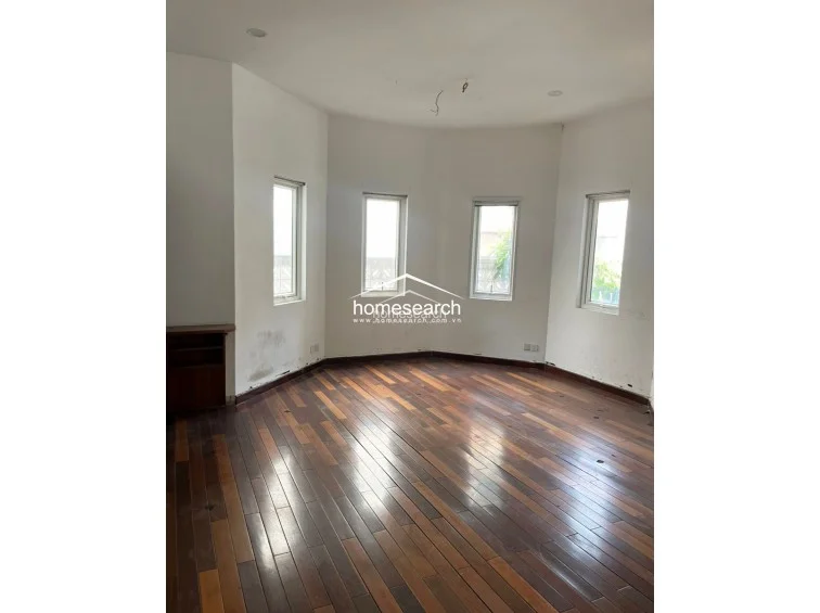 This bright, semi-circular room features warm hardwood floors and four vertical windows that provide excellent natural light and a pleasant view. The space is minimalist in design, highlighting the architectural curve of the walls and the clean, white finish, making it a versatile area for a bedroom or study.