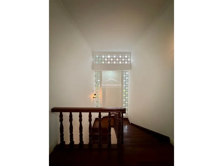 This staircase landing features a classic design with rich, dark wood flooring and a matching traditional wooden balustrade. The space is uniquely accented by decorative breeze blocks that allow for soft, diffused natural light to filter through, creating an elegant and airy atmosphere.