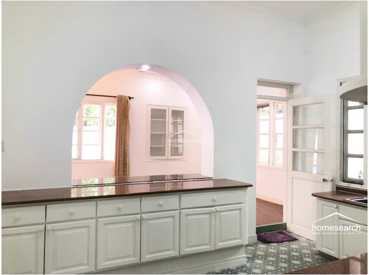 This functional kitchen area highlights a large, white cabinetry island with a dark granite countertop that serves as a breakfast bar, looking through an arched opening into the adjacent living space. The floor features intricate, patterned tiles, and the room includes a glass-paned door that provides natural light and access to the outdoors. The space is clean and well-organized, maintaining a consistent aesthetic with the rest of the home.