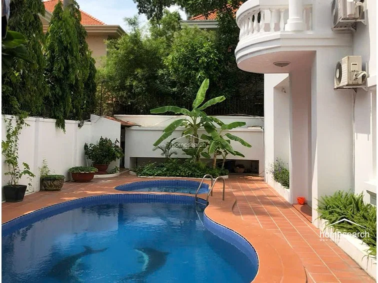 This private outdoor area features a kidney-shaped swimming pool and a separate smaller soaking pool, surrounded by terracotta-tiled decking. The space is lushly landscaped with mature tropical plants and banana trees, offering a serene, resort-like environment for relaxation.