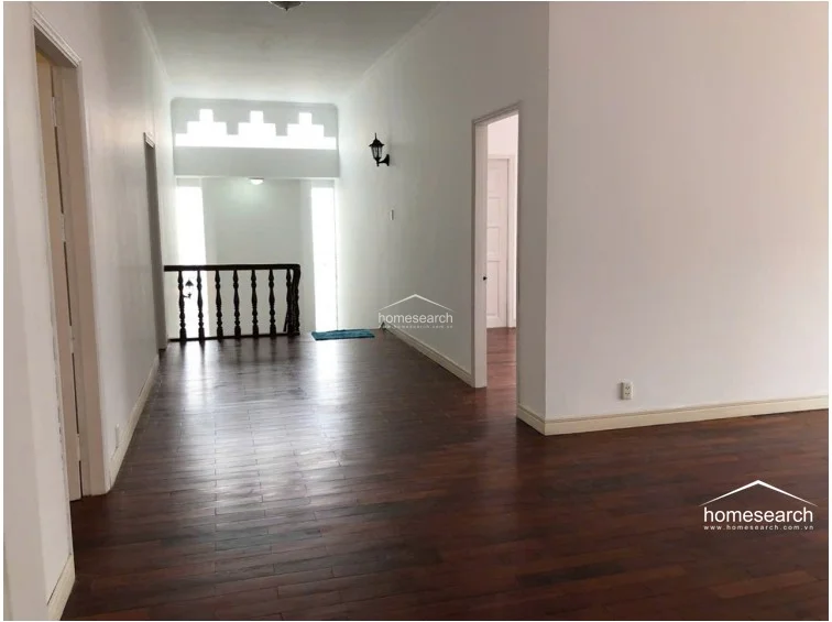 This upper-level landing or hallway connects various rooms and features a traditional wooden balustrade overlooking the space below. The area is finished with consistent hardwood flooring and white walls, accented by decorative geometric ventilation blocks that allow for natural airflow and light.