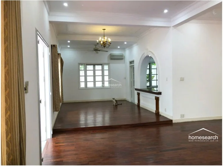 This expansive living area features a raised wooden platform section, creating a distinct transition between zones within an open-flow floor plan. Architectural interest is provided by a decorative arched pass-through, while the space is illuminated by a central chandelier and recessed lighting.