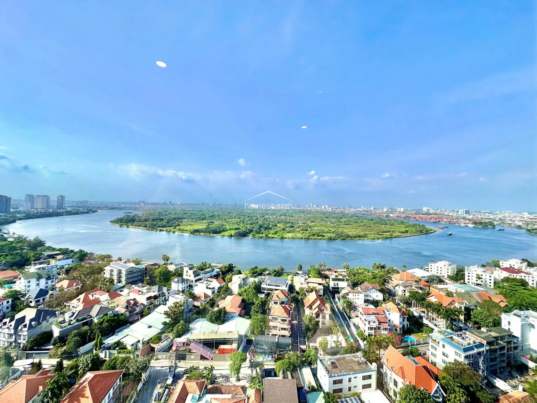 This high-angle exterior view captures a breathtaking panoramic vista of a winding river and a lush, green island. The surrounding neighborhood consists of low-rise residential buildings with terracotta roofs, highlighting the property's prime, elevated location and scenic outlook.