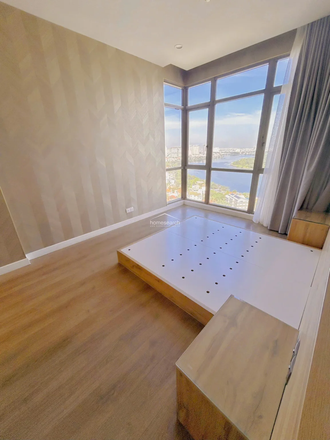 This bedroom features a custom-built low-profile wooden bed frame with integrated side tables, maximizing the floor space. The room is anchored by a striking chevron-patterned wallpaper and warm wood-look flooring, creating a sophisticated and cozy atmosphere.