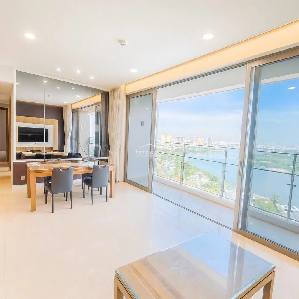 This bright living and dining area features polished light-colored tile flooring and a wall-to-wall mirror that enhances the sense of space. Large floor-to-ceiling sliding glass doors provide abundant natural light and seamless access to a balcony with expansive, panoramic river and city views.