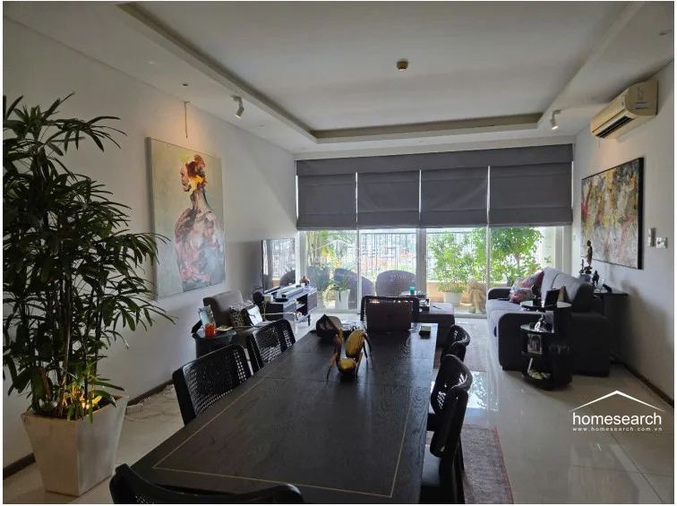 This wide-angle view captures the cohesive flow between the dining area and the living space, emphasizing the generous proportions of the room. The area is illuminated by recessed ceiling lighting and track lights, while a large potted plant adds a touch of greenery to the bright, airy atmosphere.