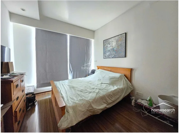 This secondary bedroom maintains a consistent aesthetic with wood-look flooring and a matching wooden bed frame, offering a cozy and functional sleeping space. It is equipped with a wooden dresser for storage and features a large window covered by grey roller blinds, ensuring privacy while allowing for adjustable natural light.