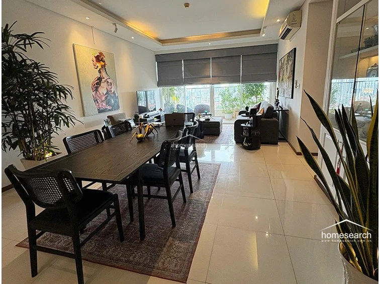 This open-plan living and dining area features polished light-colored tile flooring and a sophisticated, modern aesthetic. The space flows seamlessly toward a balcony with floor-to-ceiling glass doors, allowing for significant natural light and an expansive city view.