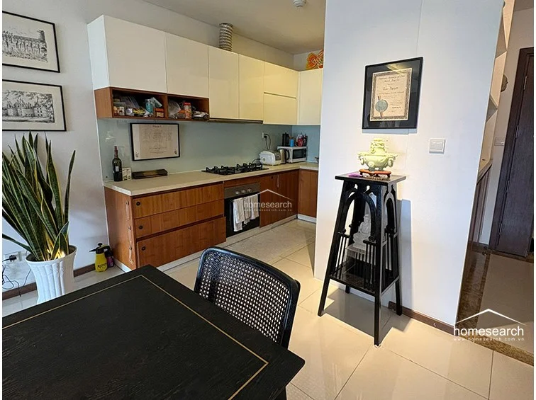 This kitchen features an L-shaped layout with a modern two-tone aesthetic, combining white upper cabinets with warm wood-toned lower cabinetry and light countertops. The space is finished with high-gloss white floor tiles and includes a built-in gas stovetop and oven, creating a functional and well-maintained cooking area adjacent to the dining space.