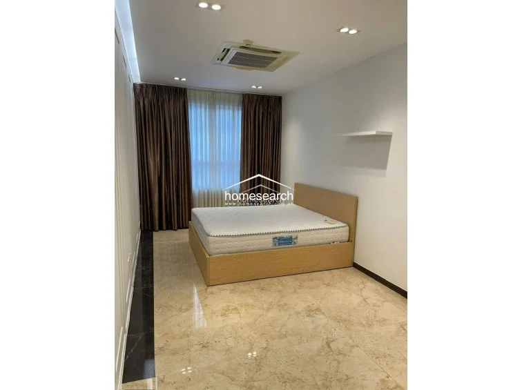 This bedroom layout provides a spacious, minimalist feel with a neutral color palette and high-quality marble flooring. The room is well-lit by recessed ceiling lights and features a large window dressed with floor-to-ceiling brown curtains for privacy and light control.