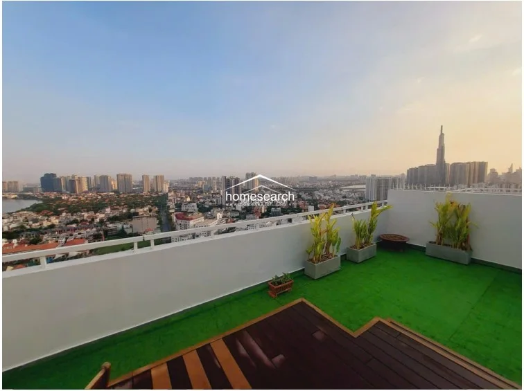 This expansive rooftop terrace offers a panoramic city view and features a mix of artificial turf and dark wood decking. The space is well-maintained with potted greenery along the perimeter, providing a clean, modern outdoor living area.