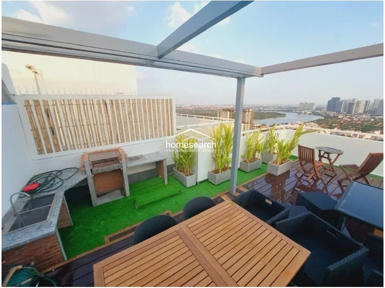 This outdoor kitchen and dining area on the terrace is equipped with a built-in grill, stone countertops, and a sink, perfect for entertaining. The space includes a wooden dining set and black wicker chairs, all sheltered by a metal pergola frame.