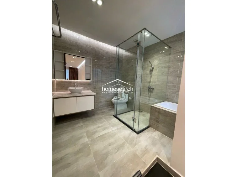 This modern bathroom features a sophisticated neutral aesthetic with large-format stone-look tiles and a floating vanity with an integrated vessel sink. The layout includes a glass-enclosed walk-in shower and a separate soaking tub, complemented by recessed LED accent lighting and a mirrored cabinet for storage. The space is in excellent condition, offering a clean, spa-like atmosphere with high-quality fixtures.