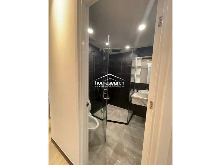 This modern bathroom features a sleek glass-enclosed walk-in shower and a contemporary vanity with a marble-topped basin. The space is finished with high-contrast dark wall tiles and lighter floor tiles, creating a sophisticated and clean look.