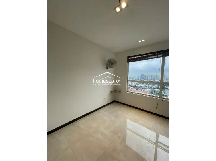 This bright, airy room offers expansive city views through a large window fitted with wooden blinds. The minimalist space features neutral walls, polished tile flooring, and a wall-mounted fan, maintaining a simple and well-maintained condition throughout.