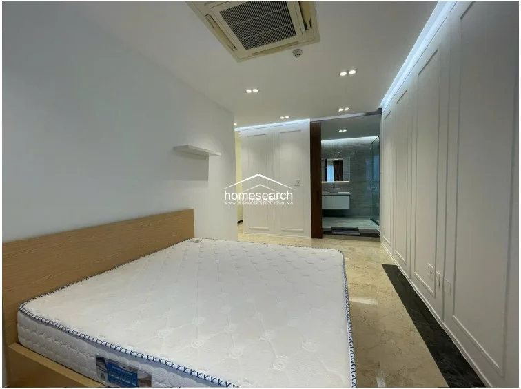 This spacious master bedroom features a neutral color palette, elegant wall paneling, and polished marble flooring that extends into the en-suite bathroom. It is equipped with a modern ceiling-mounted AC unit, recessed lighting, and a floating shelf, offering a clean and sophisticated living environment.
