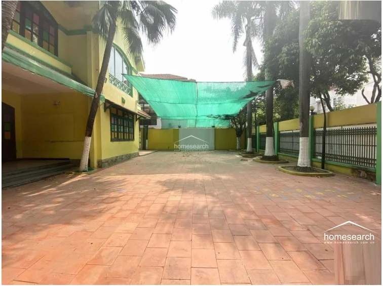 This view focuses on the expansive, tiled outdoor courtyard, showcasing the transition from the building's entrance to the open-air play zone. The yellow exterior walls, decorative stained-glass window accents, and mature palm trees create a vibrant, well-defined outdoor environment.