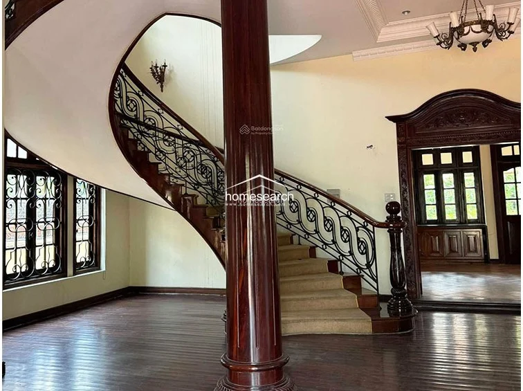 The grand foyer is defined by a striking spiral staircase with an ornate wrought-iron railing and a polished dark wood central column. The space is finished with rich hardwood flooring and a decorative chandelier, leading seamlessly into adjacent rooms through dark wood-framed doorways.
